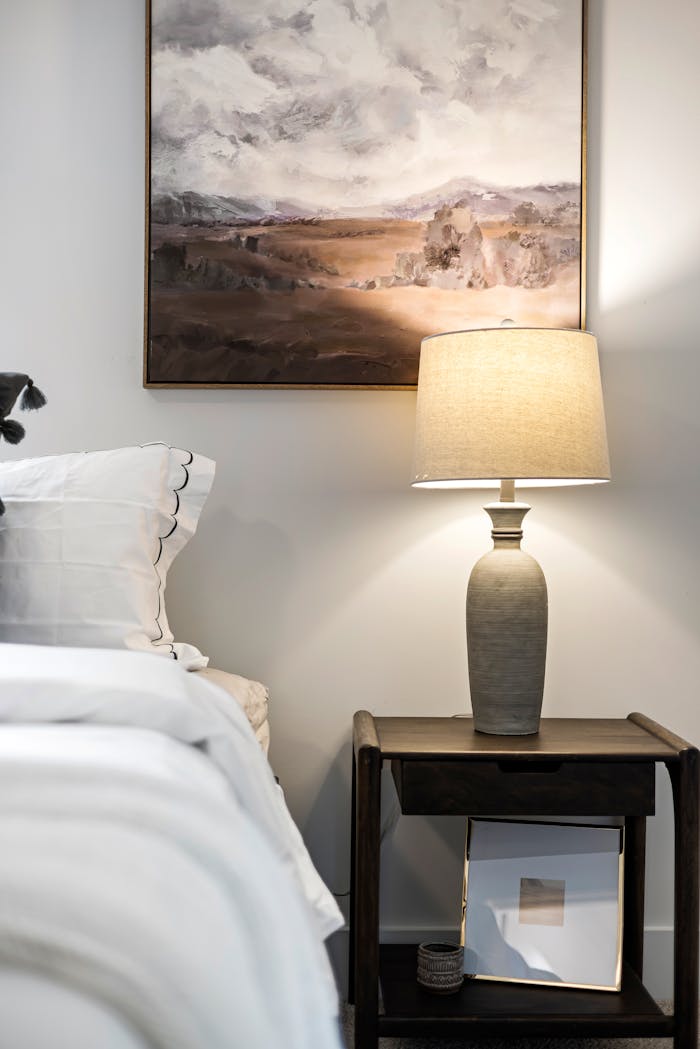 Elegant bedroom setup with bedside table and lamp under a serene painting.